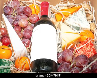 Boîte cadeau avec vin rouge couché et fruits. Présenter la boîte avec le fromage, le raisin, la mandarine et la bouteille de vin maquette dans le panier. Panier de noël gastronomique à proximité Banque D'Images