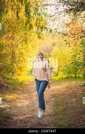 Une femme blonde avec une coupe courte de cheveux marche à travers la forêt dans un pull tricoté. Randonnée en plein air dans la forêt d'automne. Banque D'Images