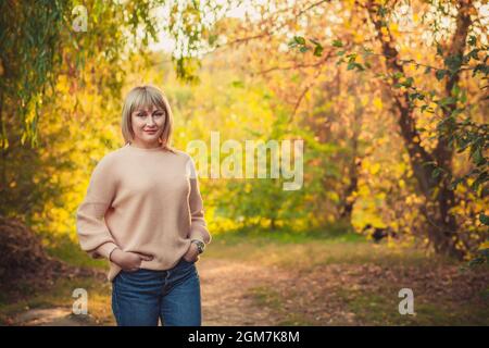 Une femme blonde avec une coupe courte de cheveux marche à travers la forêt dans un pull tricoté. Randonnée en plein air dans la forêt d'automne. Banque D'Images