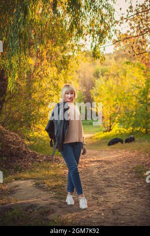 Une femme blonde avec une coupe courte de cheveux marche dans la forêt dans un pull tricoté et deux grands chiens noirs rottweiler. Randonnée en plein air dans la forêt d'automne Banque D'Images