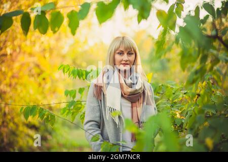 Une femme blonde avec une coupe courte passe à travers la forêt dans un manteau de laine gris et un foulard à carreaux. Marche dans la nature en forêt d'automne Banque D'Images