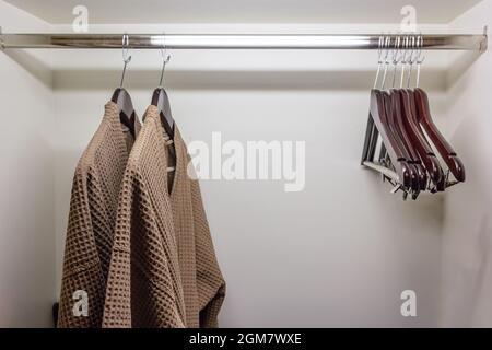 Cintres de vêtements et robe de douche brune dans la poitrine de vêtements, gros plan de cintre de vêtements et peignoir dans l'armoire de l'hôtel, peignoir suspendu sur le rack. Ça, je Banque D'Images