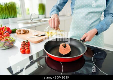 Vue rognée d'une jolie femme expérimentée préparant un plat naturel steak de saumon verser de l'huile à la maison cuisine blanche claire Banque D'Images