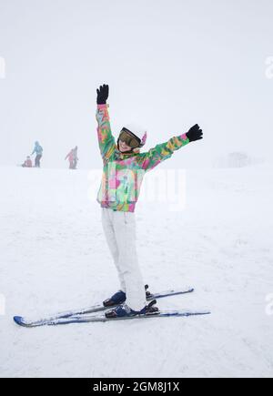 belle fille de 16 ans dans une humeur gaie est de skier sur un flanc de montagne avec ses mains vers le haut. Des vacances d'hiver intéressantes Banque D'Images