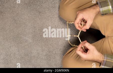 rosaire entre les mains. homme musulman priant après la prière sur tapis gris. vue de dessus. espace pour le texte Banque D'Images