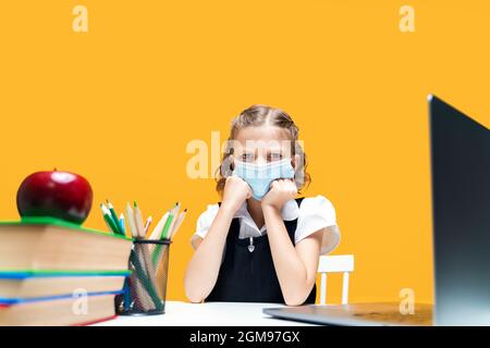 Triste fille d'école caucasienne en colère portant un masque médical étudiant à la maison avec un ordinateur portable. Formation à distance Banque D'Images