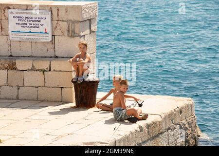 Prvic Sepurin, Croatie - 25 août 2021 : enfants blonds assis au soleil sur la jetée en pierre de pêche et regardant au loin, et une mer derrière Banque D'Images