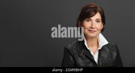Portrait de femme d'âge moyen et bien-regardant. Femme portant une chemise blanche et une veste en cuir noir sur fond solide foncé. Studio portrait féminin. Bil Banque D'Images