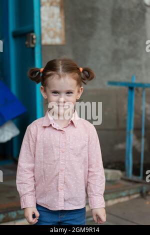 Cool mignon redhead petite fille dans une chemise avec deux queues de cheval se tient contre le fond de la porte de la maison Banque D'Images