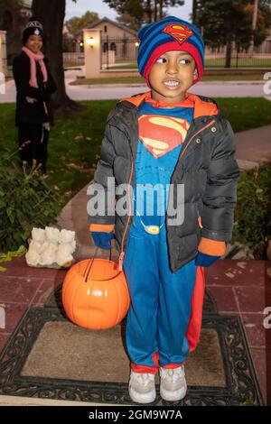 10-31-2017 Tulsa USA - jeune garçon noir habillé en costume de super-homme avec panier de bonbons de potiron et veste debout à la porte de trick r en se traitant avec la mère Banque D'Images