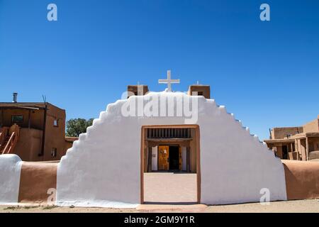 La boue Adobe pueblo mission church avec porte à plaza courtyard peint en blanc et porte d'entrée montrant à travers la mission avec d'autres bâtiments d'adobe à bac Banque D'Images