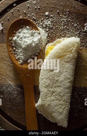 Tapioca, un plat typiquement brésilien, avec garniture de mozzarella sur une planche à découper et une cuillère en bois remplie de farine. Plat à base de farine. Banque D'Images