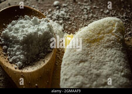 Tapioca, un plat typiquement brésilien, avec garniture de mozzarella sur une planche à découper et une cuillère en bois remplie de farine. Plat à base de farine. Banque D'Images