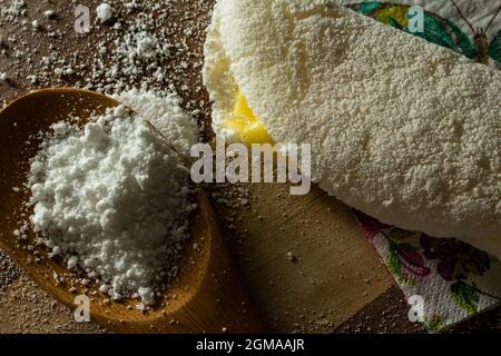 Tapioca, un plat typiquement brésilien, avec garniture de mozzarella sur une planche à découper et une cuillère en bois remplie de farine. Plat à base de farine. Banque D'Images