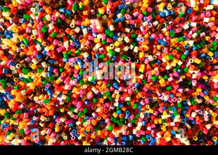 Petites perles en plastique colorées formant un arrière-plan éclatant. Ensemble de petits éléments artisanaux multicolores et éclatants. Banque D'Images