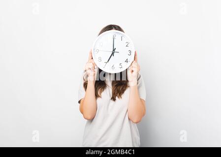 Femme vêtue de blanc tient et couvre le visage avec une horloge murale ronde. Banque D'Images