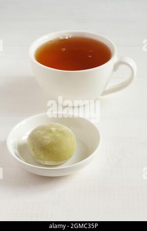 Thé vert matcha dessert japonais mochi sur une soucoupe blanche et une tasse de thé vert sur une table en bois blanc. Gros plan Banque D'Images