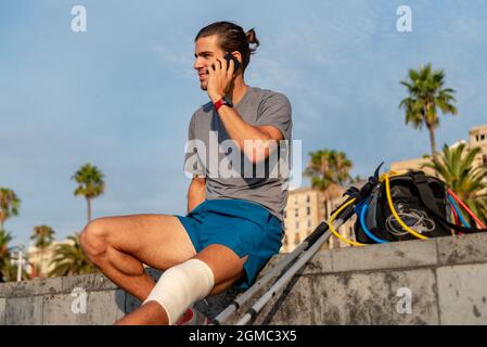 Jeune latin homme avec des béquilles en utilisant le téléphone portable après avoir fait de l'exercice Banque D'Images