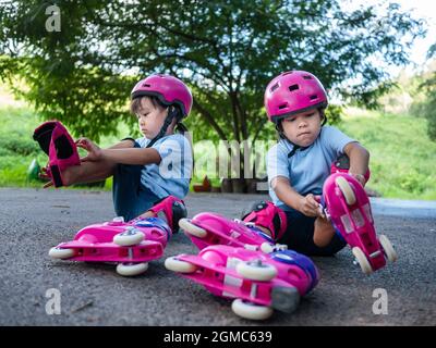 Deux sœurs sœurs portent des coussinets de protection et un casque de sécurité s'exerçant à patiner à roulettes dans la rue du parc. Sports d'extérieur actifs pour les enfants. Banque D'Images