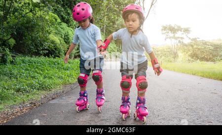 Deux sœurs sœurs portent des coussinets de protection et un casque de sécurité s'exerçant à patiner à roulettes dans la rue du parc. Sports d'extérieur actifs pour les enfants. Banque D'Images