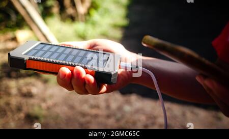 Un bloc d'alimentation mobile rechargeable avec panneaux solaires dans les mains des jeunes femmes, en gros plan. Connecté à un téléphone portable, une tablette ou un téléphone intelligent et en charge Banque D'Images