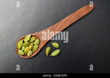 Vue de dessus de cardamome dans cuillère en bois sur fond noir texturé Banque D'Images