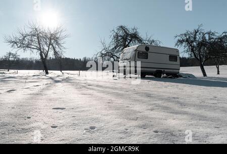 Paysage d'hiver avec une camionnette de camping garée dans un verger enneigé. Paysage d'hiver ensoleillé avec le sol couvert de neige et le ciel bleu. Banque D'Images