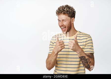 Beau blond homme se démène et montre les pouces dans l'approbation, louange vous, félicitant gagnant, debout sur fond blanc Banque D'Images