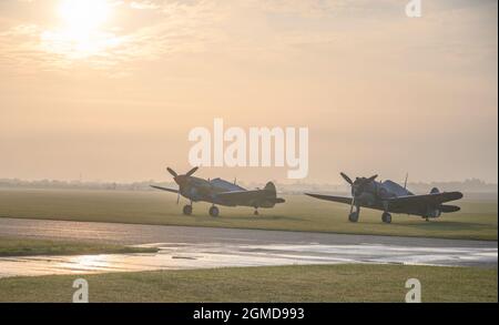 IWM Duxford, Cambridgeshire, Royaume-Uni. 18 septembre 2021. Un début malin alors que le spectacle aérien de la bataille de Grande-Bretagne aura lieu du 18-19 au 22 septembre à IWM Duxford, L'ancien site de la RAF qui a joué un rôle central dans certains des jours les plus dramatiques de l'histoire du XXe siècle - servant de base à de nombreux pilotes de Spitfire et d'ouragan pendant la Seconde Guerre mondiale. Image: The Fighter Collection Curtiss P-40F Warhawk et Curtis Hawk 75 s'assoient sur l'aérodrome brumeux au lever du soleil. Crédit : Malcolm Park/Alay Live News Banque D'Images