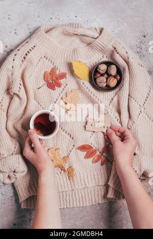 Mains de femme tenant une tasse de thé et carte de voeux bonjour automne. Pull beige confortable. Banque D'Images