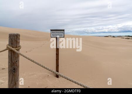 Poste de clôture en bois et corde avec un panneau de non intrusion dans la réserve naturelle des dunes de sable immaculées de Slowinski Naitonal Park écrit en polonais et en anglais Banque D'Images