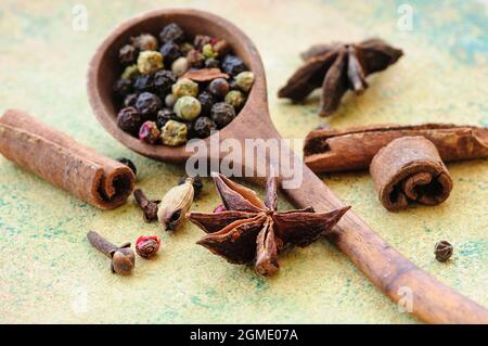 Encore la vie de grains de différents poivrons dans une cuillère en bois, étoiles anis, bâtons de cannelle et clous de girofle. Mise au point sélective. Macro. Banque D'Images