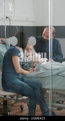 Parents inquiets assis avec une fille malade attendant l'expertise de la maladie pendant l'examen médical dans la salle d'hôpital. Enfant portant un tube nasal à oxygène tenant un ours en peluche lorsqu'il est au lit Banque D'Images