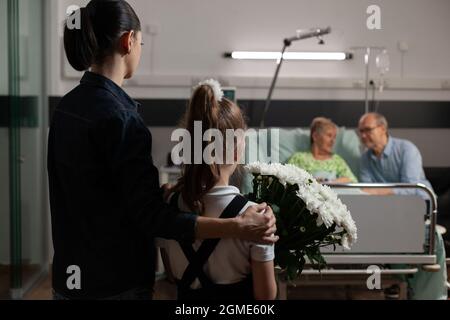Petite-fille soignante qui apporte des fleurs à une grand-mère âgée malade qui la rend visite à l'hôpital pendant la thérapie clinique. Famille gaie soutenant la femme âgée pendant le rétablissement de la maladie Banque D'Images