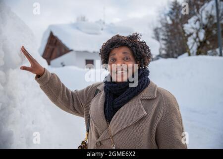 Portrait d'une femme africaine souriante d'âge moyen dans les montagnes en hiver avec beaucoup de neige, elle porte un manteau et une écharpe Banque D'Images