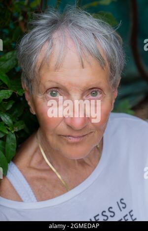 Femme mûre regardant la caméra. Femme de chambre souriante dans son jardin. Gros plan sur le visage de la femme. Portrait du modèle féminin posé sur l'appareil photo à l'extérieur Banque D'Images