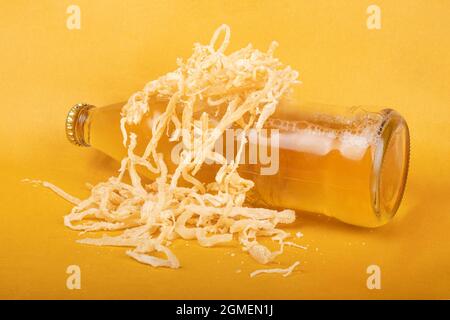 une bouteille de bière légère avec calamar séché sur fond jaune. Banque D'Images