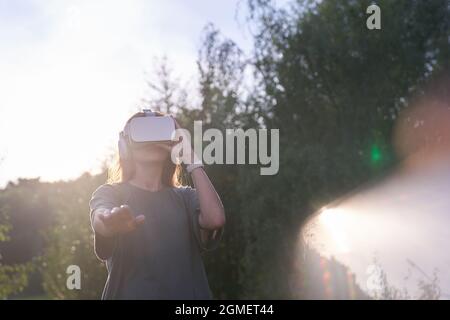 Une fille tenant des lunettes de réalité virtuelle sur sa tête avec ses mains. Il s'étire d'une main jusqu'à la caméra, à côté d'un faisceau de lumière du soleil. Photo de haute qualité Banque D'Images