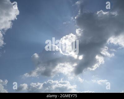 Soleil au-dessus derrière les nuages dans le ciel bleu avec des rayons de lumière provenant de derrière les nuages Banque D'Images