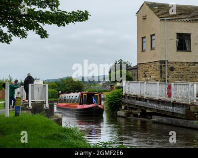 Les gens regardent louer un bateau à rames qui passe devant et traverse le pont marécageux Micklethwaite, barrières ouvertes - Leeds Liverpool Canal, Yorkshire, Angleterre, Royaume-Uni. Banque D'Images