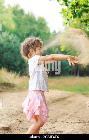 Cute Little girl jouer avec du sable dans le parc un jour d'été au coucher du soleil. Banque D'Images