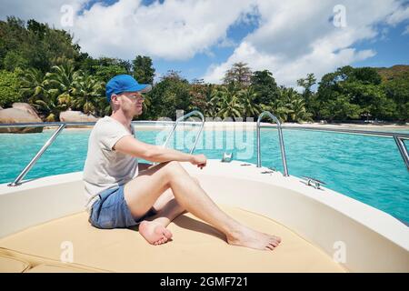 Homme reposant sur un bateau contre une belle plage de sable blanc avec des palmiers. Anse Lazio, Seychelles. Banque D'Images