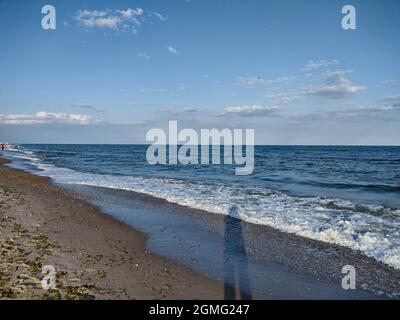 L'ombre d'un homme tombant sur les vagues bleues approchant du sable marin Banque D'Images