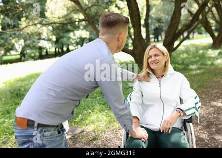 Un jeune homme fournit un soutien et des promenades dans le parc avec une femme en fauteuil roulant Banque D'Images