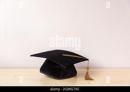 Casquette universitaire avec pampille sur une table en bois près d'un mur pastel Banque D'Images