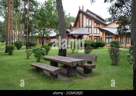 Une grande table et deux bancs de rondins bruts dans un parc d'été. Maisons en bois en arrière-plan Banque D'Images