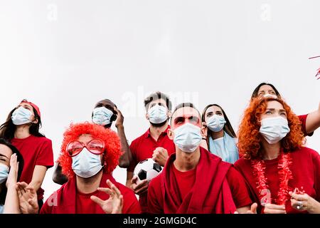 Des amis multiraciaux dans un masque facial protecteur soutenant leur équipe dans le stade Banque D'Images