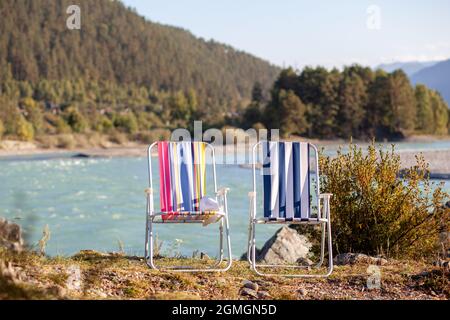 Chaises pliantes sur la rive d'une rivière de montagne par une belle journée chaude. Un endroit calme et calme pour se détendre et réfléchir. L'équipement et le repos d'un touriste. Banque D'Images