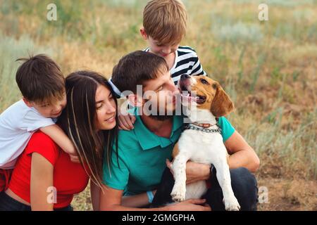Groupe de quatre familles ayant du plaisir à jouer avec Beagle chien de race pure dans un cadre rural. Portrait authentique Père, mère, deux fils et animal de compagnie. Animaux et amitié Banque D'Images