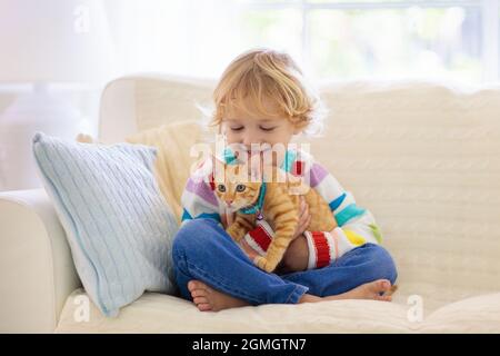 Enfant jouant avec le chat. Enfant tenant un chaton. Un petit garçon se blottant un animal de compagnie mignon assis sur un canapé dans le salon ensoleillé à la maison. Les enfants jouent avec les animaux de compagnie. Banque D'Images